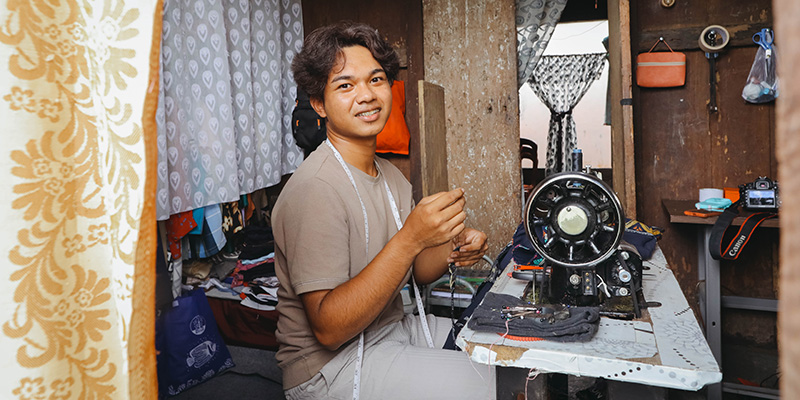 Julio uit Indonesië zit achter zijn naaimachine.