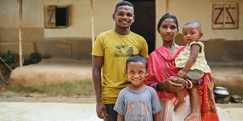 Nilkontho en Janata uit Bangladesh staan samen met hun kinderen Johan en Sohana voor hun huis. 