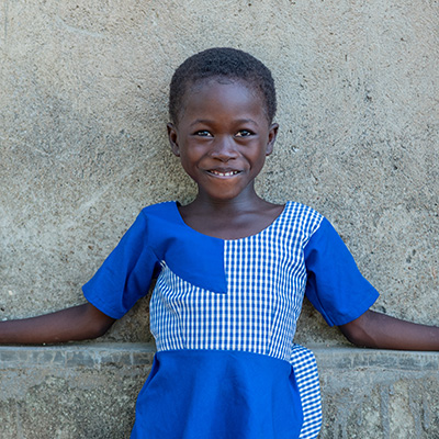 Dorcas uit Burkina Faso staat voor een muur en kijkt lachend in de camera.
