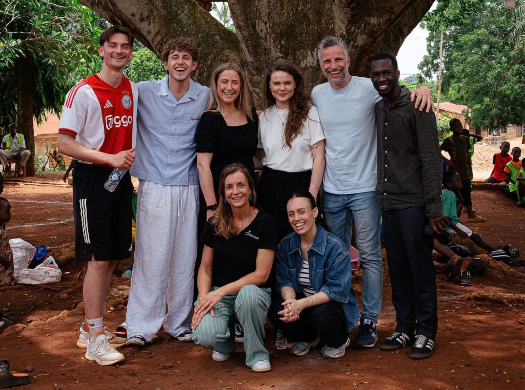 Een groep Nederlandse influencers is samen met Compassion op reis naar Togo en poseert daar voor een boom.