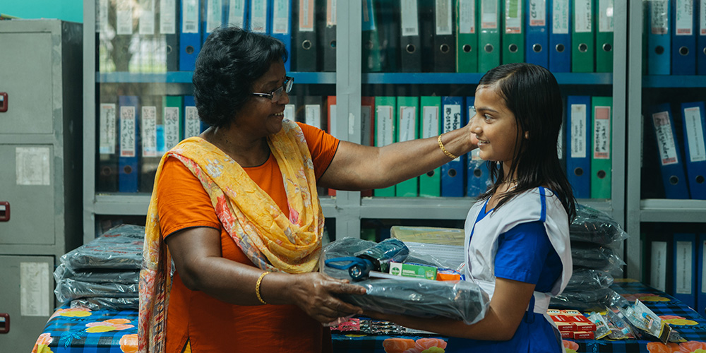 Anonna uit Bangladesh krijgt schoolspullen van een Compassion-medewerker.