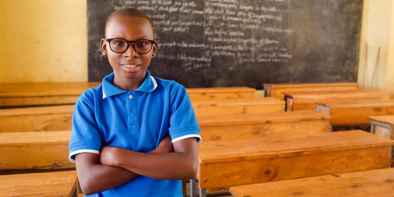 Egide uit Rwanda poseert met zijn nieuwe bril in een klaslokaal.
