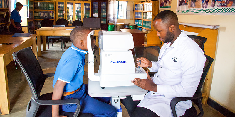 Oogarts Emmanuel uit Rwanda onderzoekt de ogen van Egide op het Compassion-project.