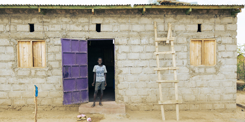 Auru uit Kenia staat in de deuropening van zijn huis en lacht naar de camera.