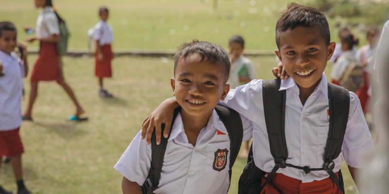 Jendri en zijn vriendje staan in hun schooluniform op een grasveld bij hun school.